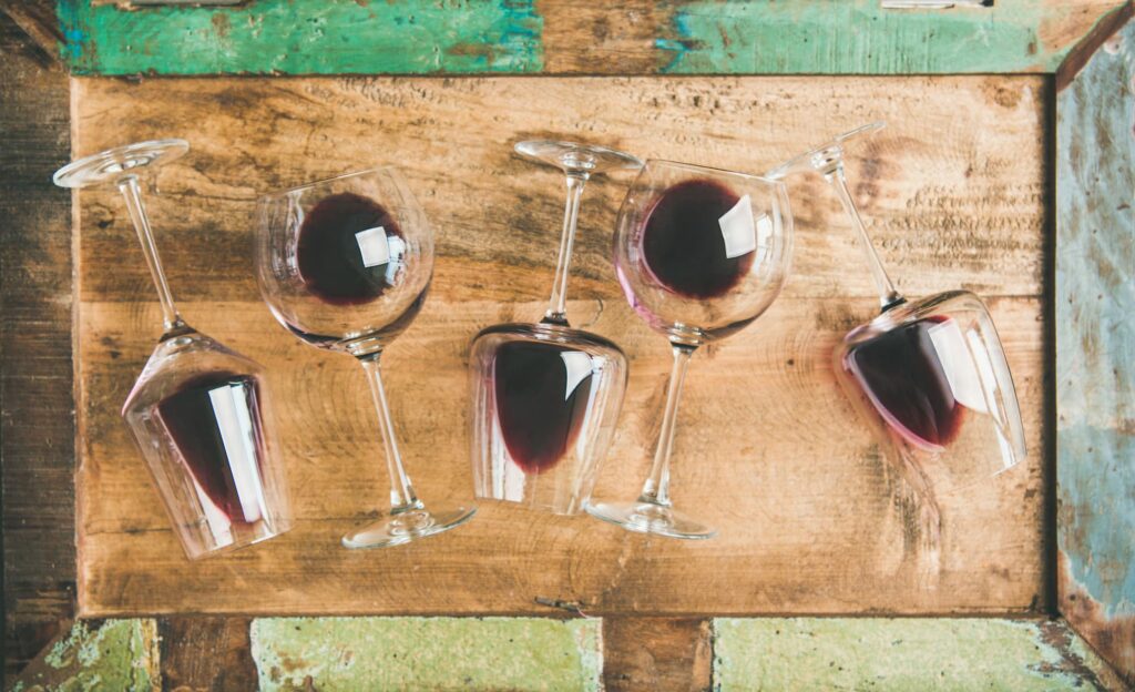 Vier Weingläser mit Rotwein, liegend auf einem rustikalen Holzbrett