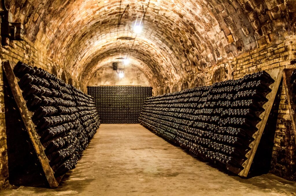 Gewölbekeller, in dem viele Flaschen Winzersekt in Rüttel-Vorrichtungen stehen.