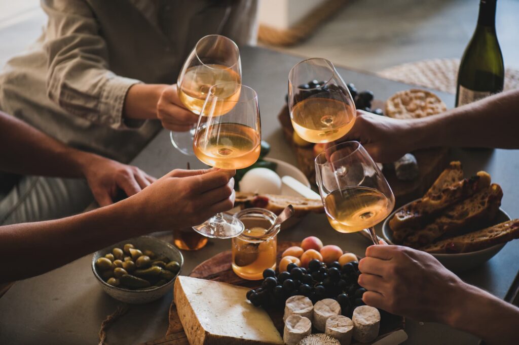 Mehrere Leute stoßen mit Weißwein an, dazu eine Käseplatte