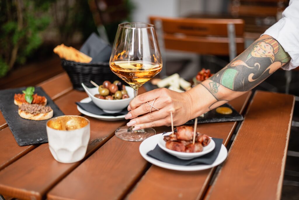 Verschiedene Antipasti auf einem Tisch, in die Mitte wird ein Glas Wein gestellt