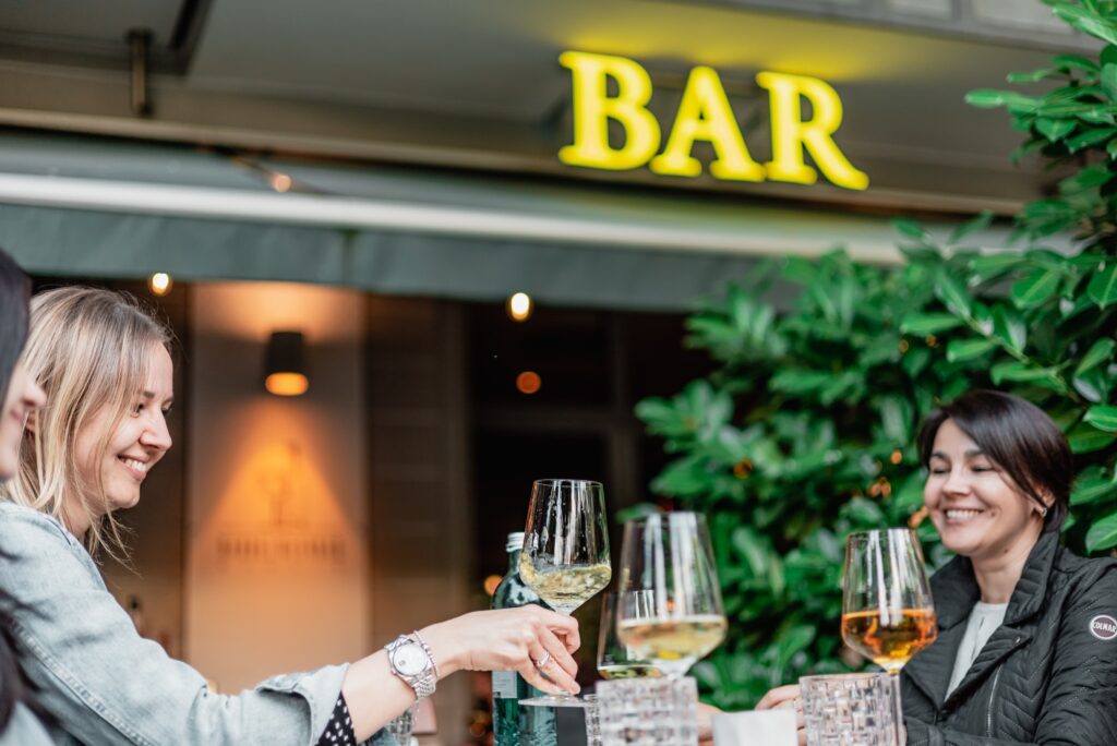 Drei rauen sitzen auf der Terrasse der Barrel Winebar und stoßen mit Weingläsern an