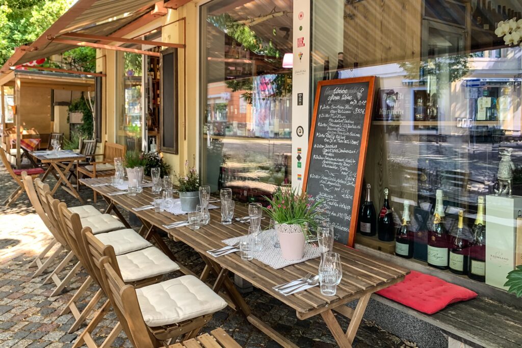 Ein langer Tisch auf der Terrasse ist eingedeckt, dahinter mehr Tische und eine Tafel mit Empfehlungen