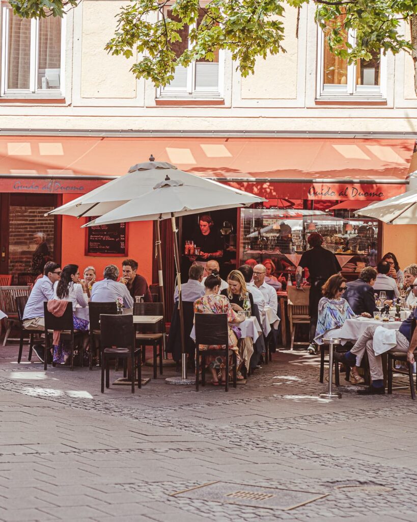 Blick von draußen auf das Guido al Duomo, auf der Terrasse sitzen viele Menschen, die einen Wein genießen