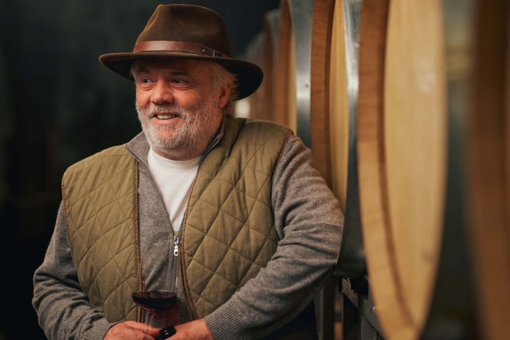 Thomas Seeger im Portrait. Er trägt einen braunen Hut und hält ein Glas Wein in der Hand