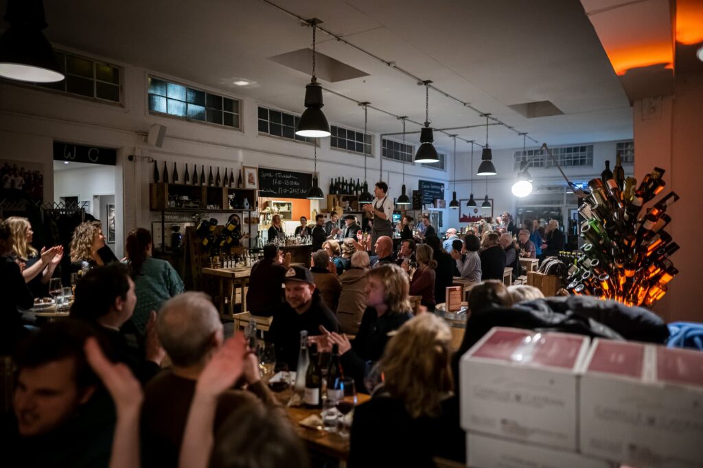 Vineyard Hamburg, Innenraum. An den Tischen sitzen viele Leute und genießen ein Glas Wein