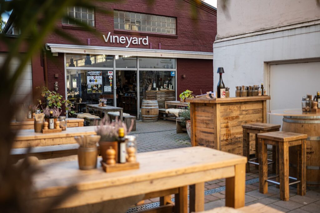 Vineyard Hamburg, Außenbereich. Draufsicht auf das Restaurant, davor einige Tische aus massivem Holz