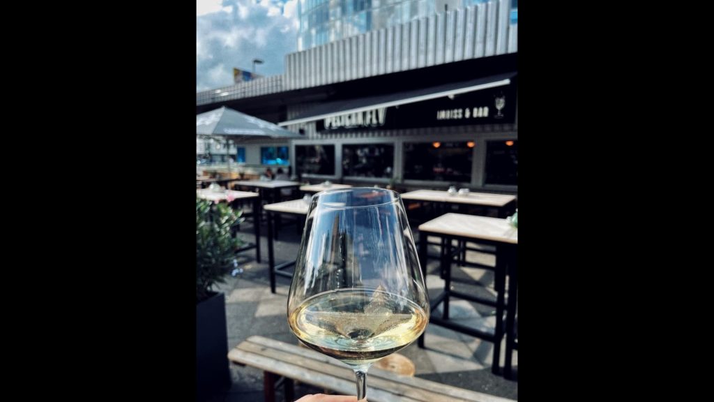 Fokus auf einem Glas Wein, dahinter das Pelican Fly