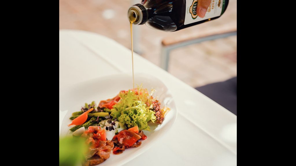 Olivenöl wird über einen Salat auf einem Teller geschüttet